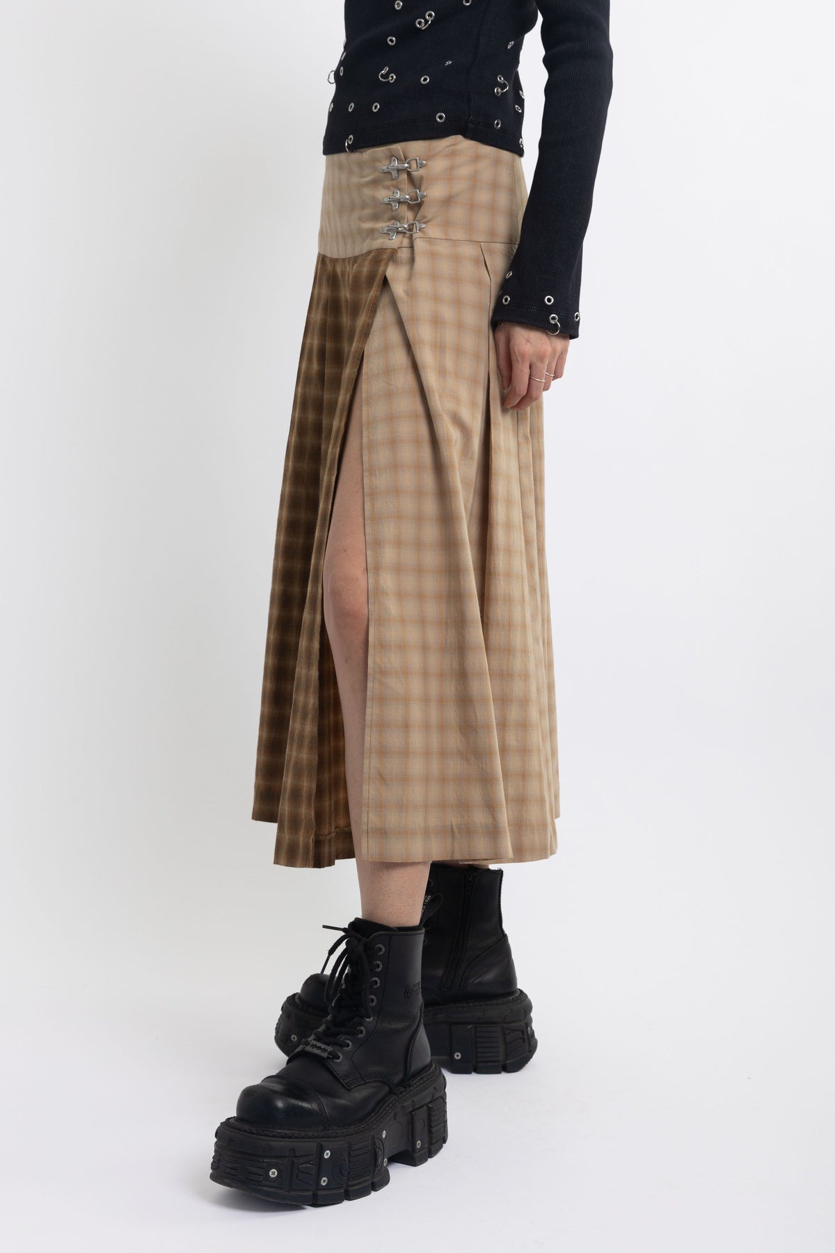 Spliced check pleated kilt midi skirt with silver clasp detail and thigh high split, worn by model