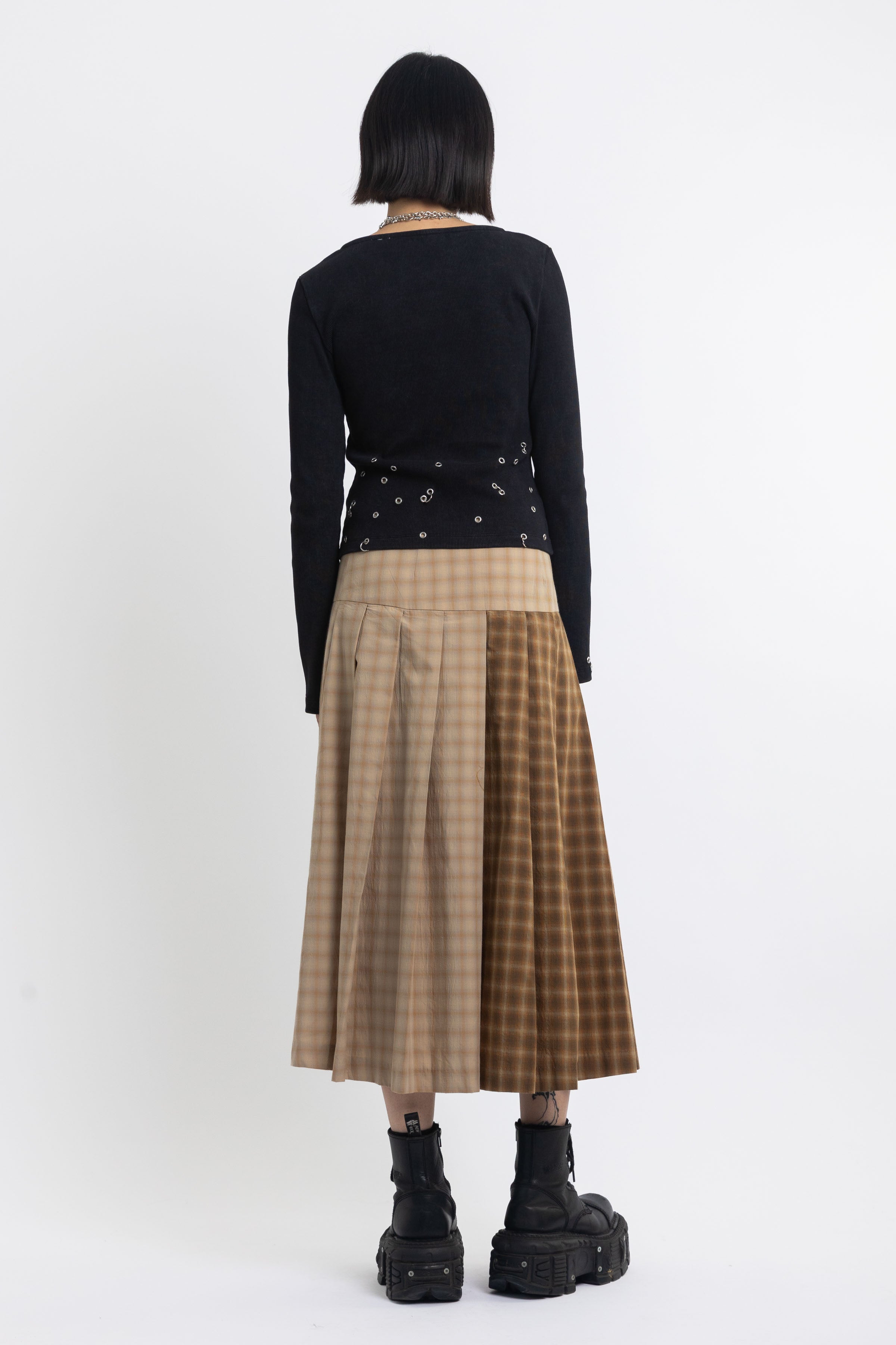 Spliced check pleated kilt midi skirt with silver clasp detail and thigh high split, worn by model