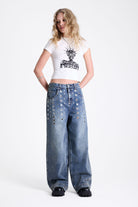 Vintage wash oversized baggy colossus jeans with silver eyelet and stud hardware detail, worn by model