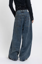 Mid blue wash ultra baggy colossus jeans with silver stud and eyelet hardware, worn by model