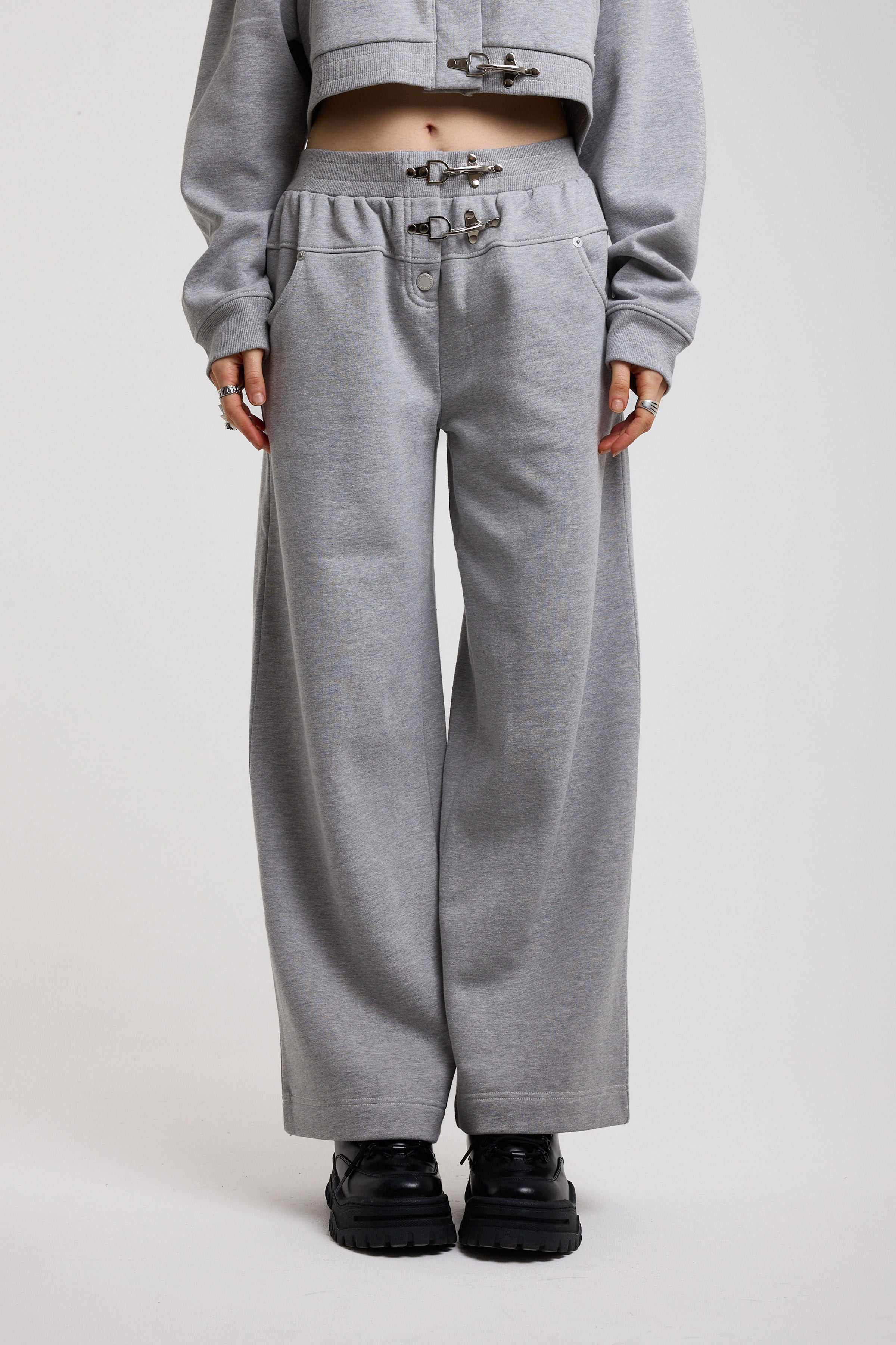 Grey wide leg trackpants with silver hardware clasp detail, worn by model