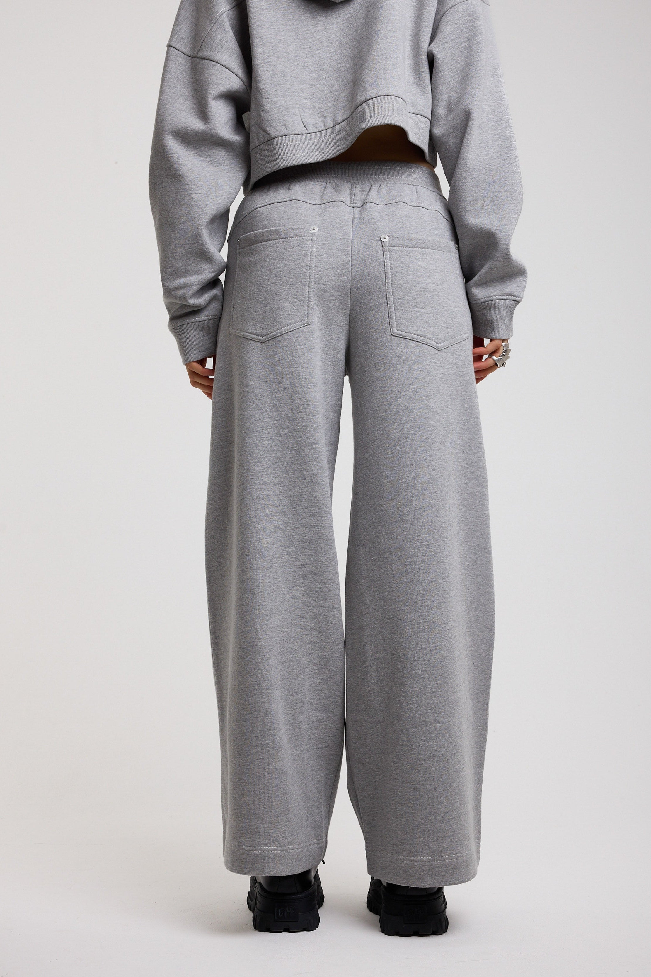 Back image of grey wide leg trackpants with silver hardware clasp detail, worn by model