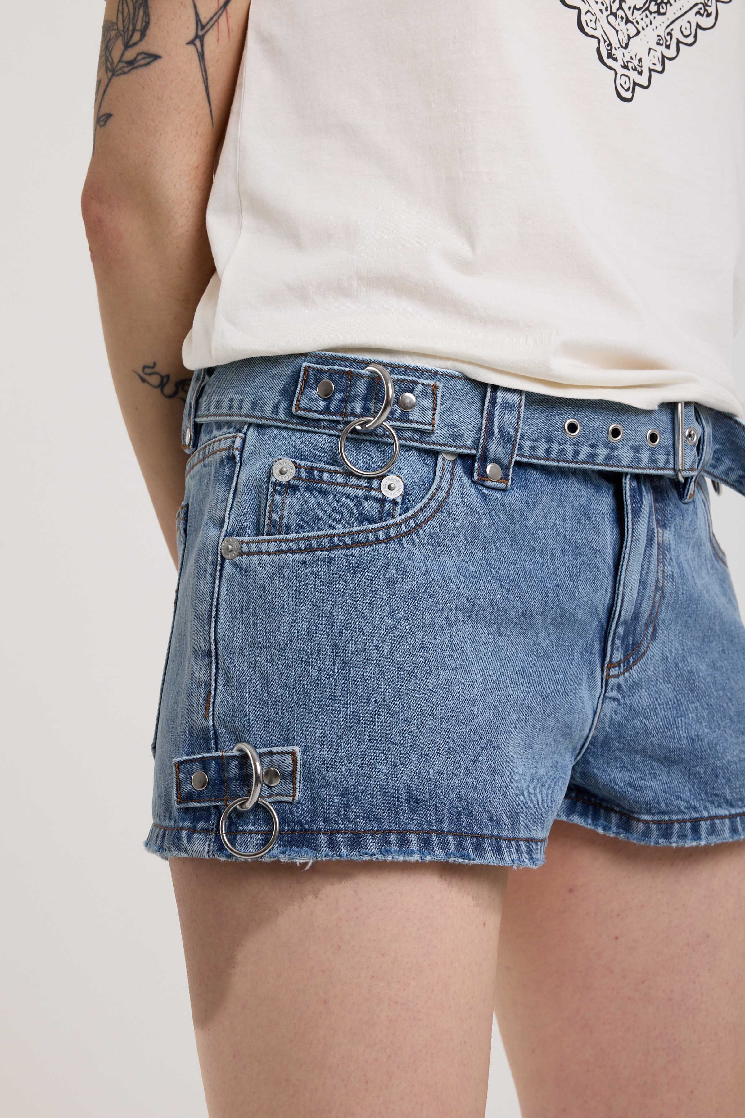 Close up of silver hardware and eyelet detail belt on light blue denim hotpants, worn by model