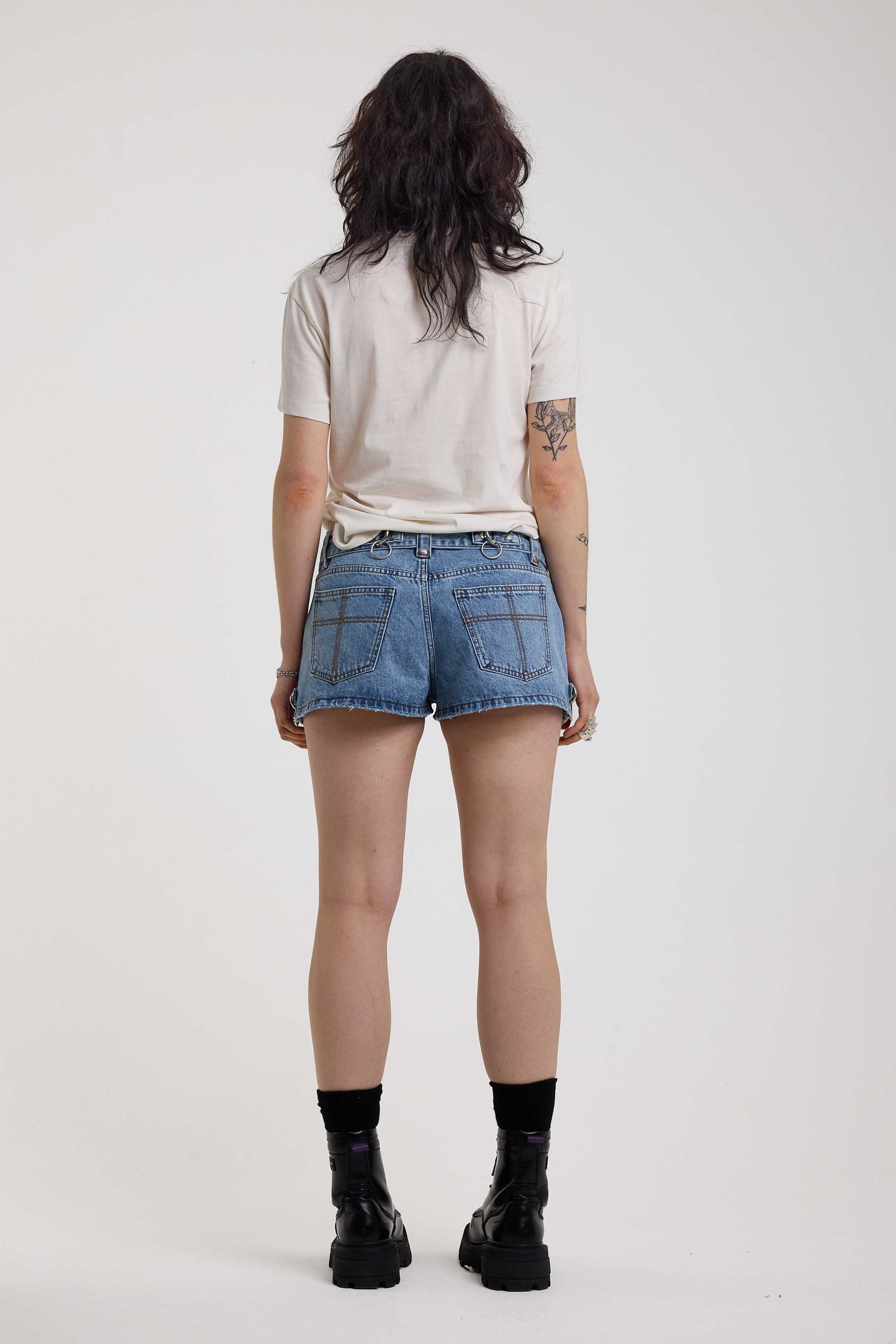 Light blue denim hotpants with silver D ring hardware and studded eyelet belt, worn by model