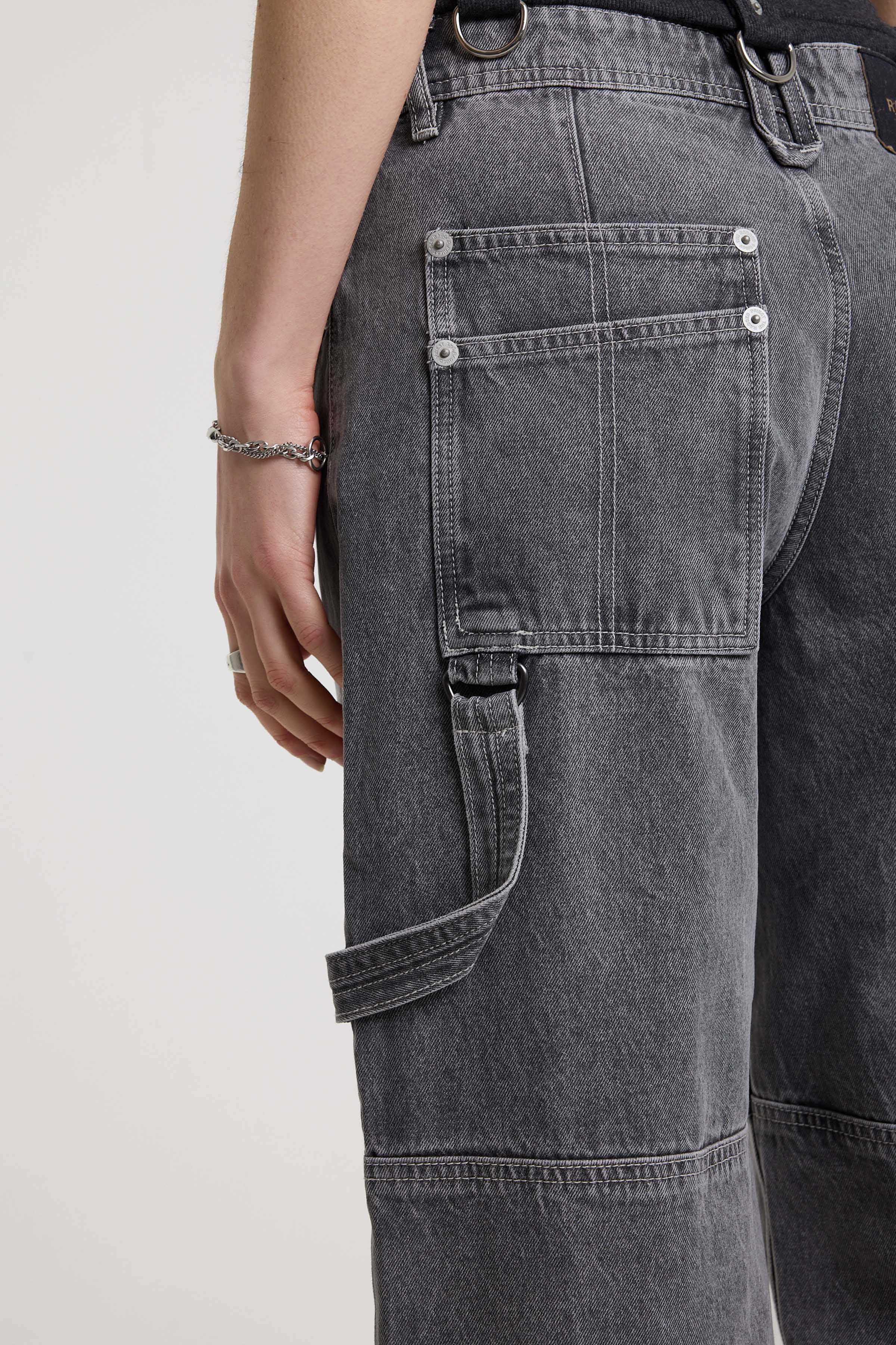 Close up showing carpenter loop on washed grey baggy cropped capri jeans with hardware detail, worn by model