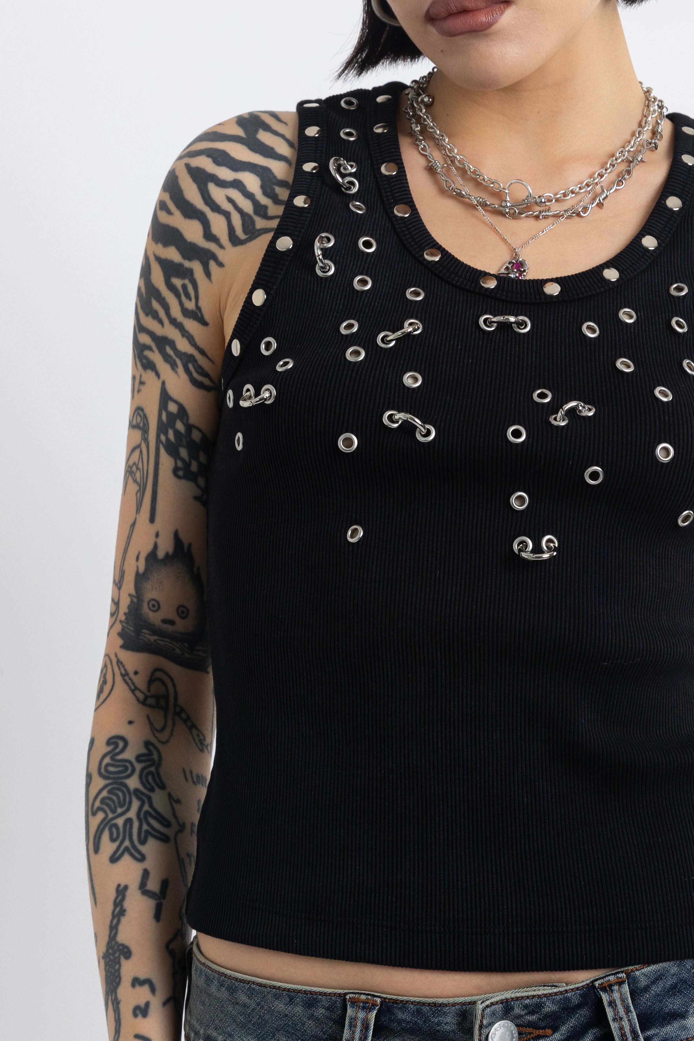 Black tank top with silver eyelets and stud hardware, worn by model