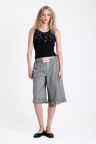 Black ribbed tank top with piercing and stud hardware details, worn by a model