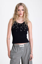 Black ribbed tank top with piercing and stud hardware details, worn by a model