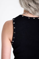 Black ribbed tank top with piercing and stud hardware details, worn by a model