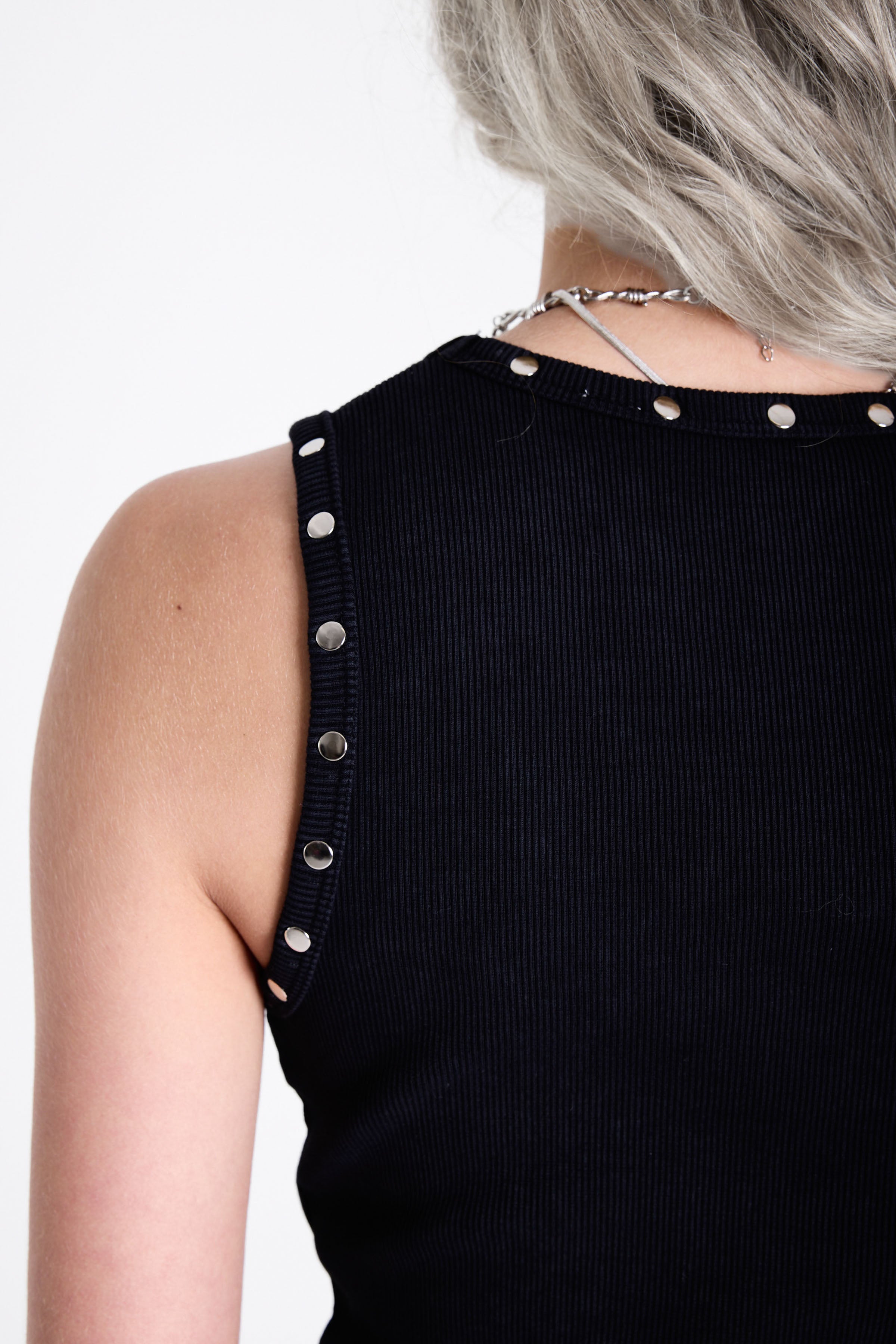 Black ribbed tank top with piercing and stud hardware details, worn by a model