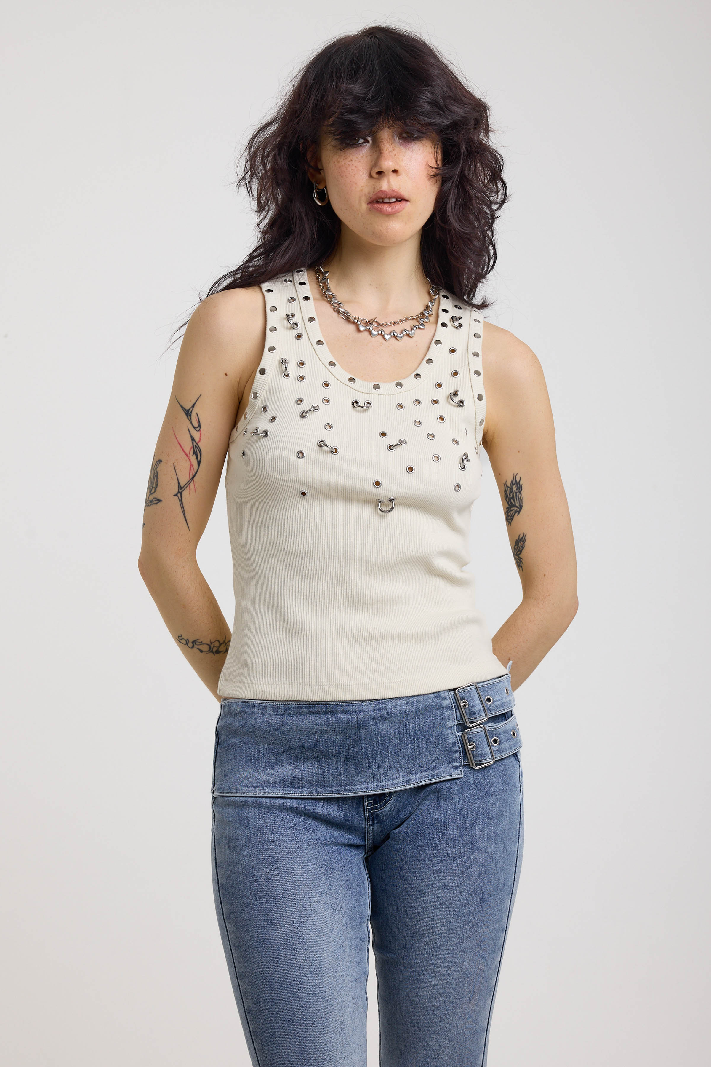 Ecru ribbed tank top with piercing and stud hardware details, worn by a model