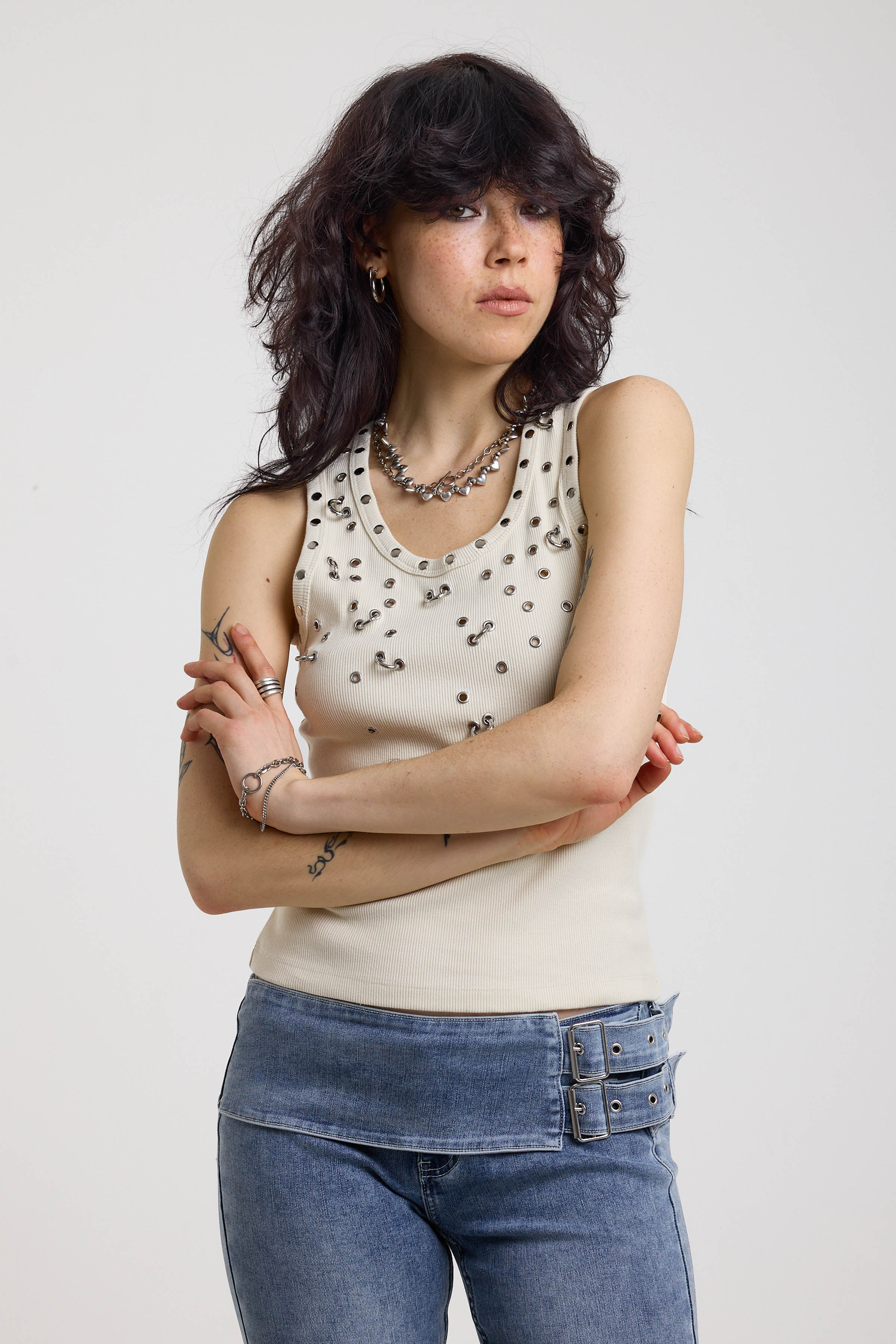 Ecru ribbed tank top with piercing and stud hardware details, worn by a model