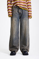 Dirty wash oversized baggy colossus jeans with silver and bronze stud hardware detail, worn by model
