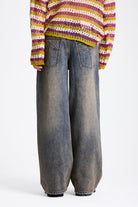Dirty wash oversized baggy colossus jeans with silver and bronze stud hardware detail, worn by model