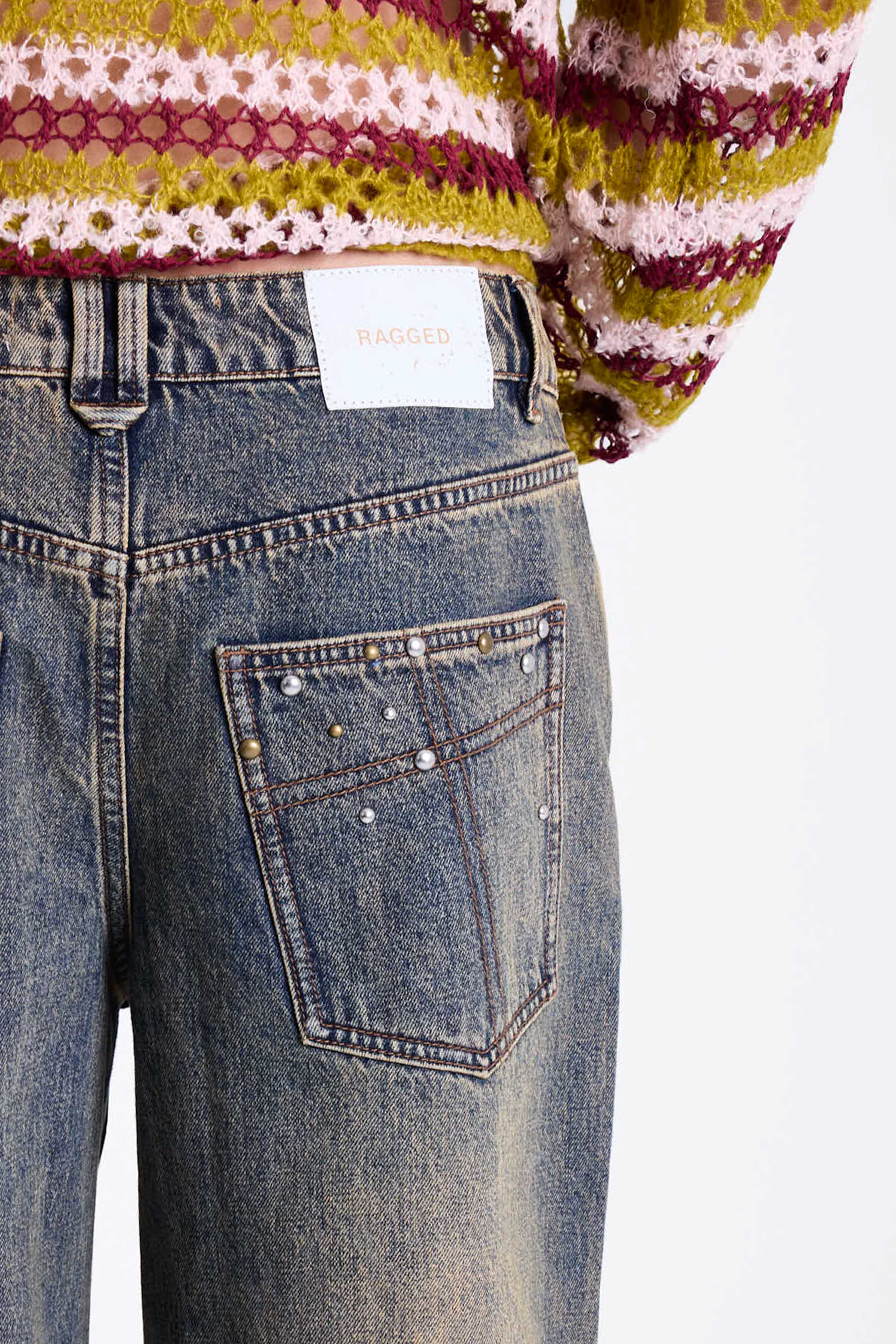 Dirty wash oversized baggy colossus jeans with silver and bronze stud hardware detail, worn by model