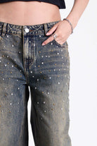 Dirty wash oversized baggy colossus jeans with silver and bronze stud hardware detail, worn by model