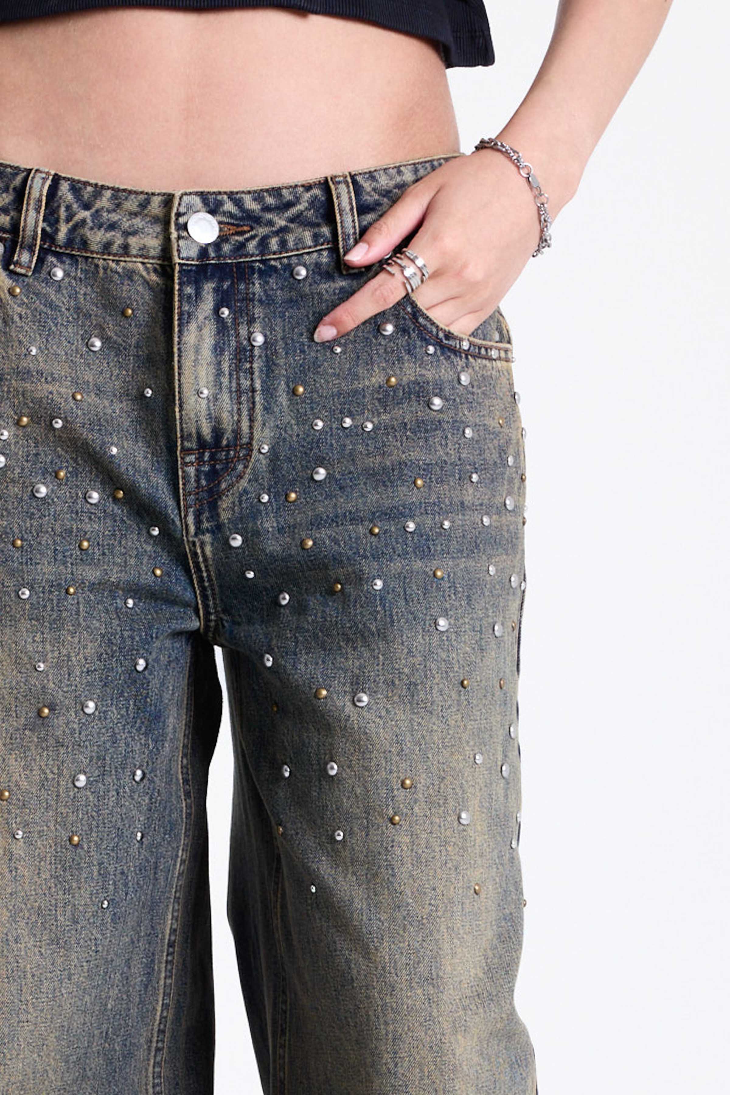 Dirty wash oversized baggy colossus jeans with silver and bronze stud hardware detail, worn by model