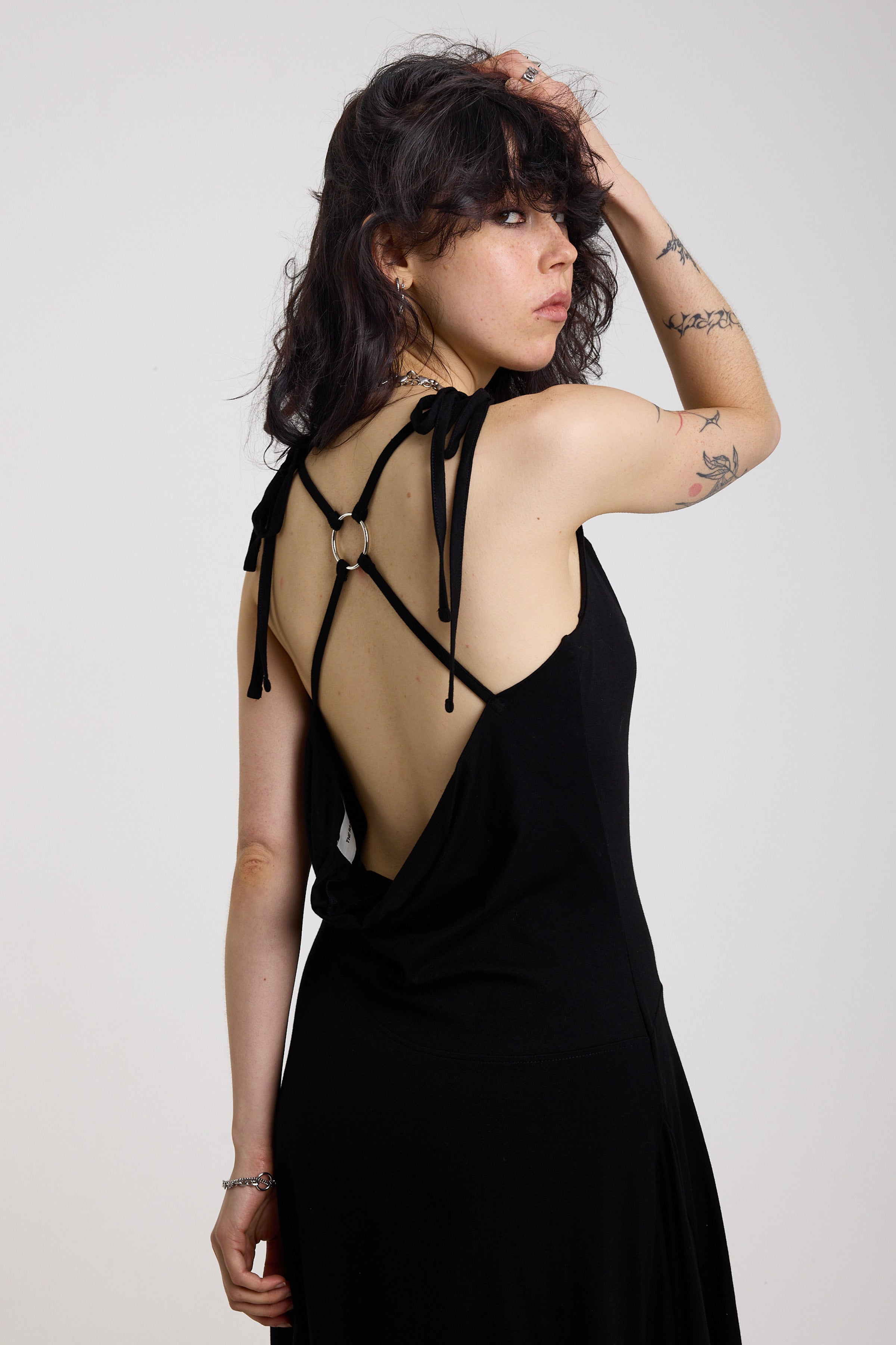 Black slinky midi maxi dress with cowl neck, draped open back, silver O-rings and strappy tie straps, worn by model