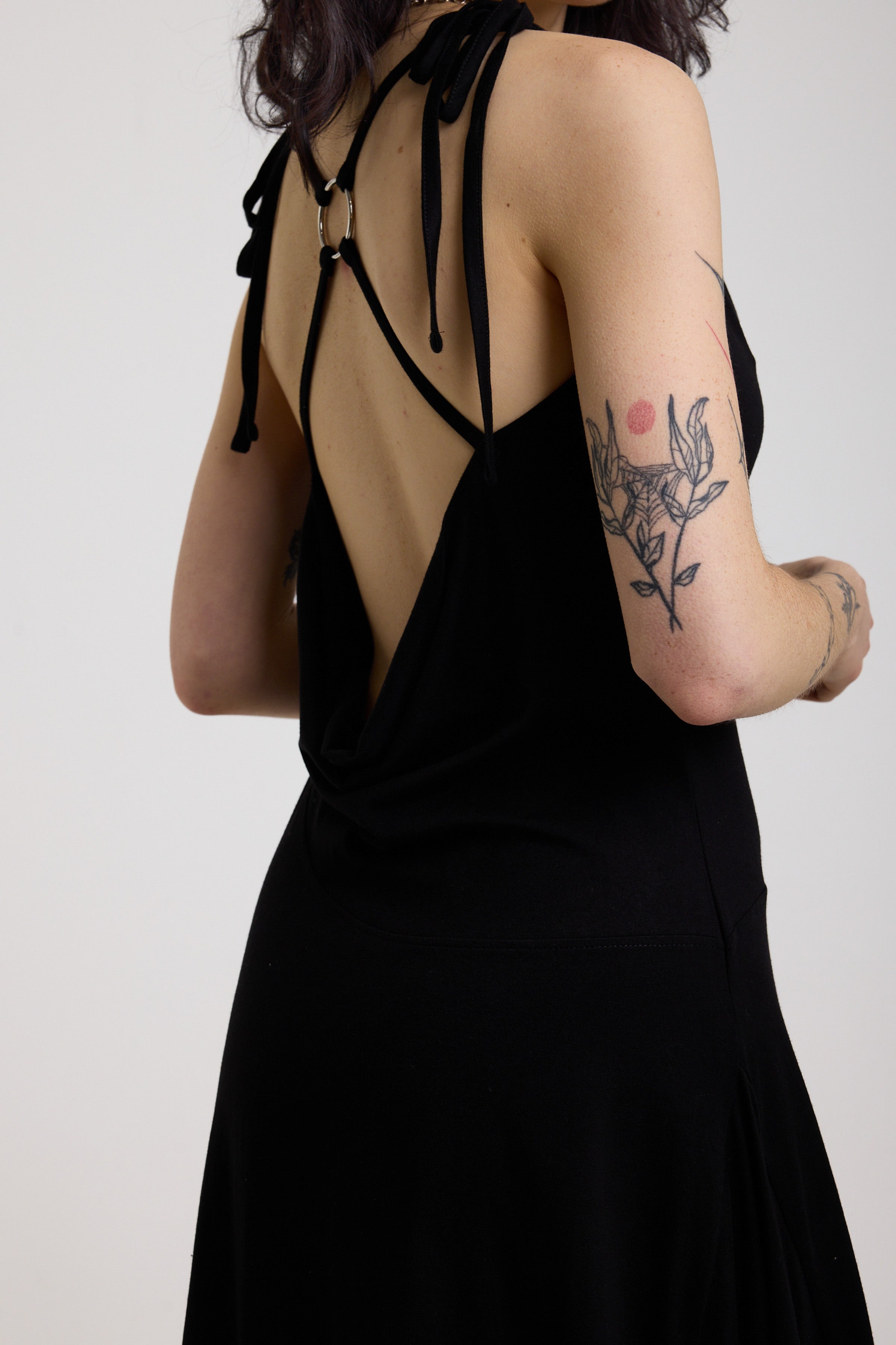 Black slinky midi maxi dress with cowl neck, draped open back, silver O-rings and strappy tie straps, worn by model