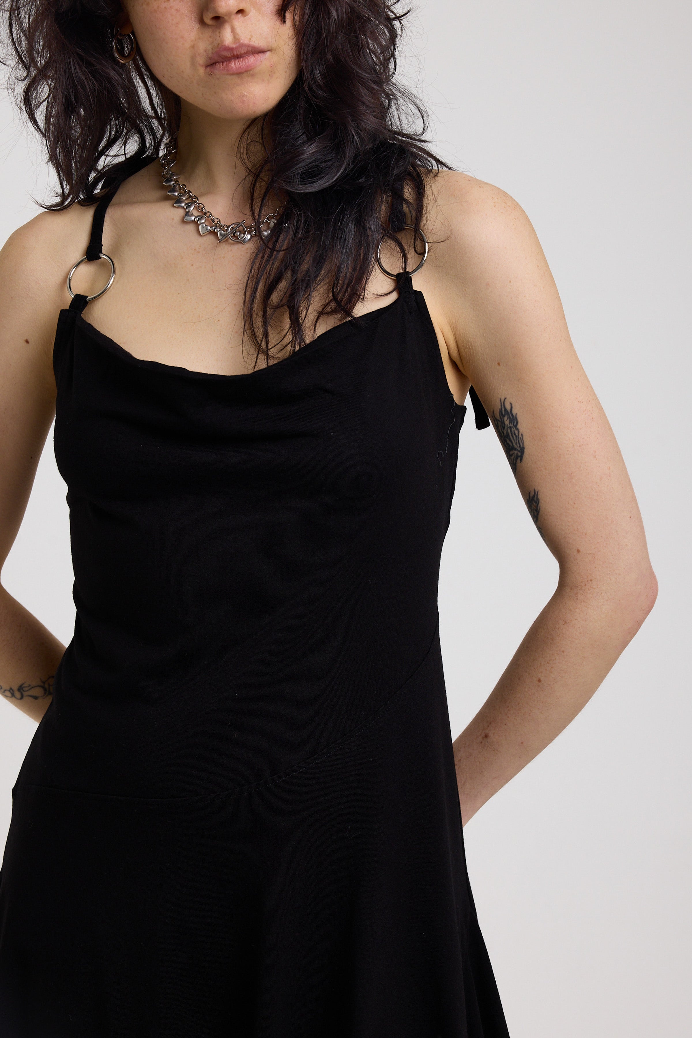 Black slinky midi maxi dress with cowl neck, draped open back, silver O-rings and strappy tie straps, worn by model