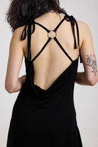 Black slinky midi maxi dress with cowl neck, draped open back, silver O-rings and strappy tie straps, worn by model