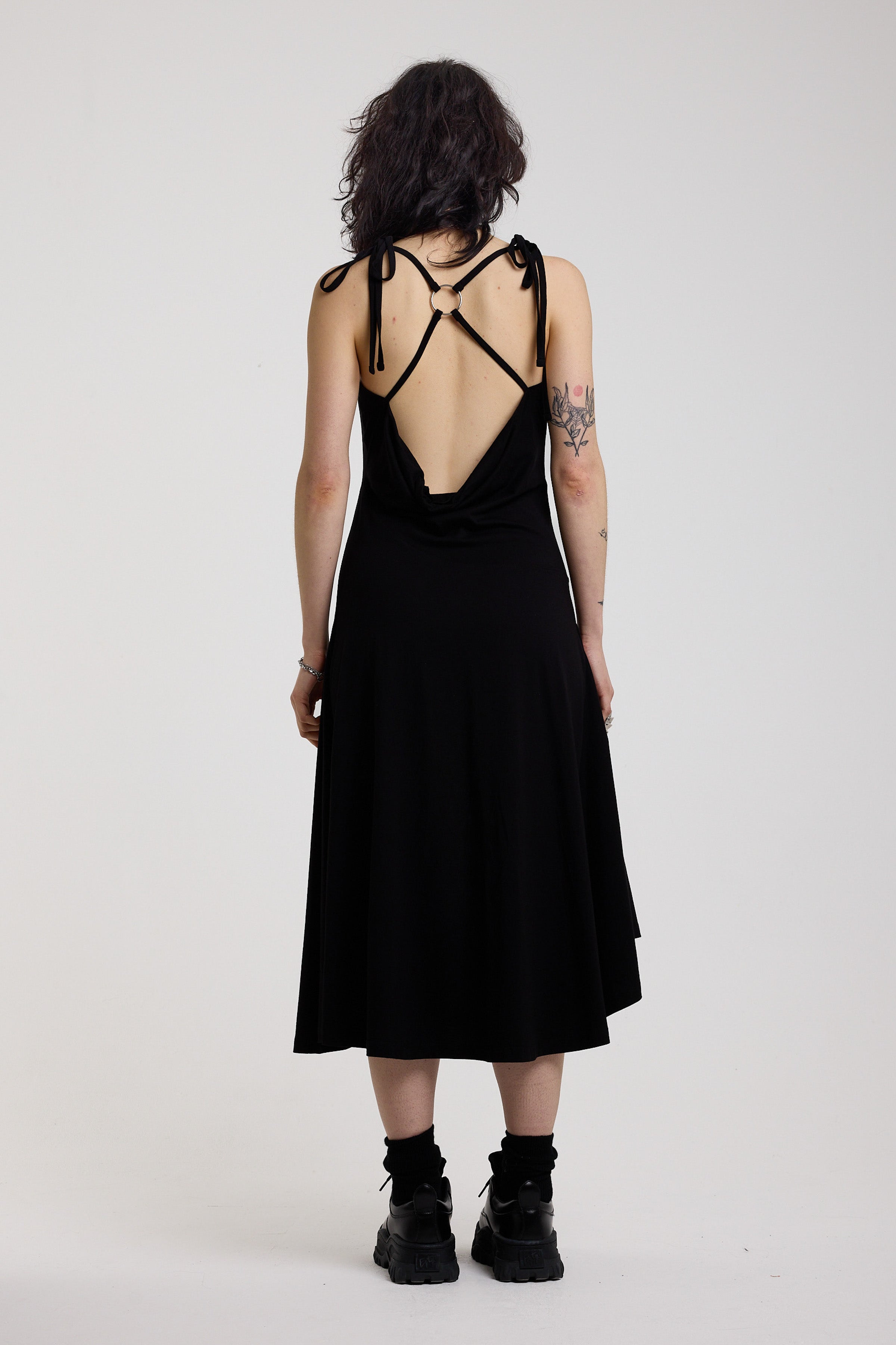 Black slinky midi maxi dress with cowl neck, draped open back, silver O-rings and strappy tie straps, worn by model