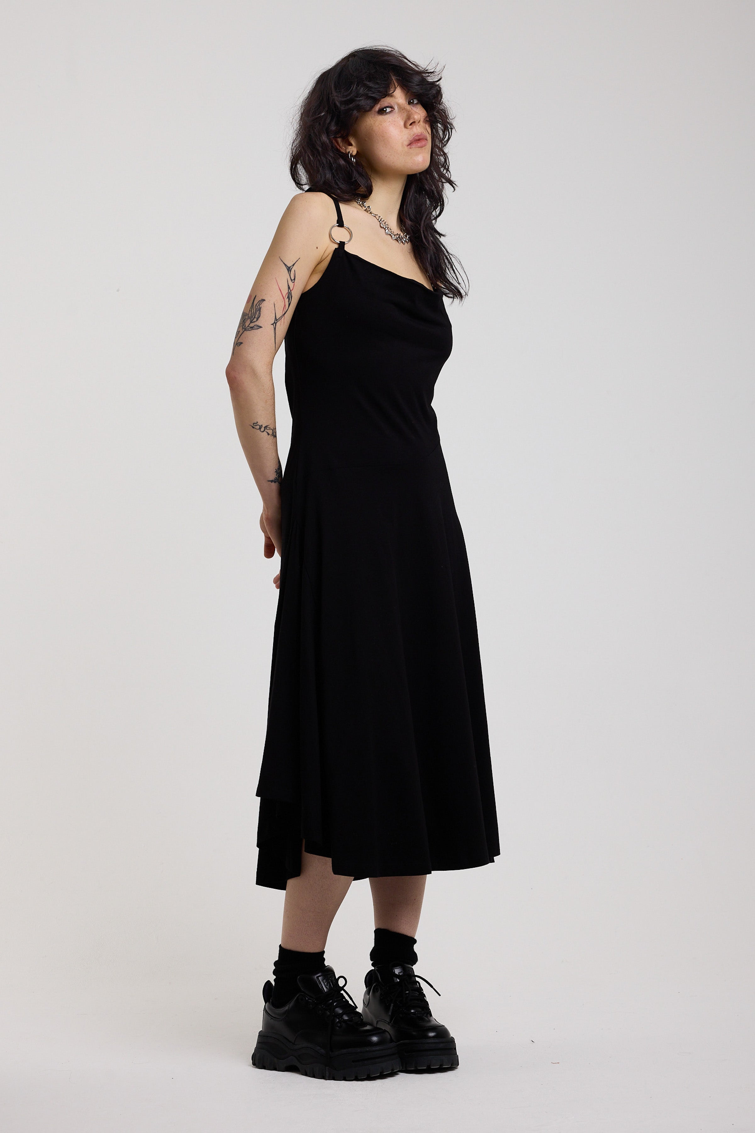 Black slinky midi maxi dress with cowl neck, draped open back, silver O-rings and strappy tie straps, worn by model