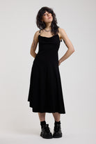 Black slinky midi maxi dress with cowl neck, draped open back, silver O-rings and strappy tie straps, worn by model