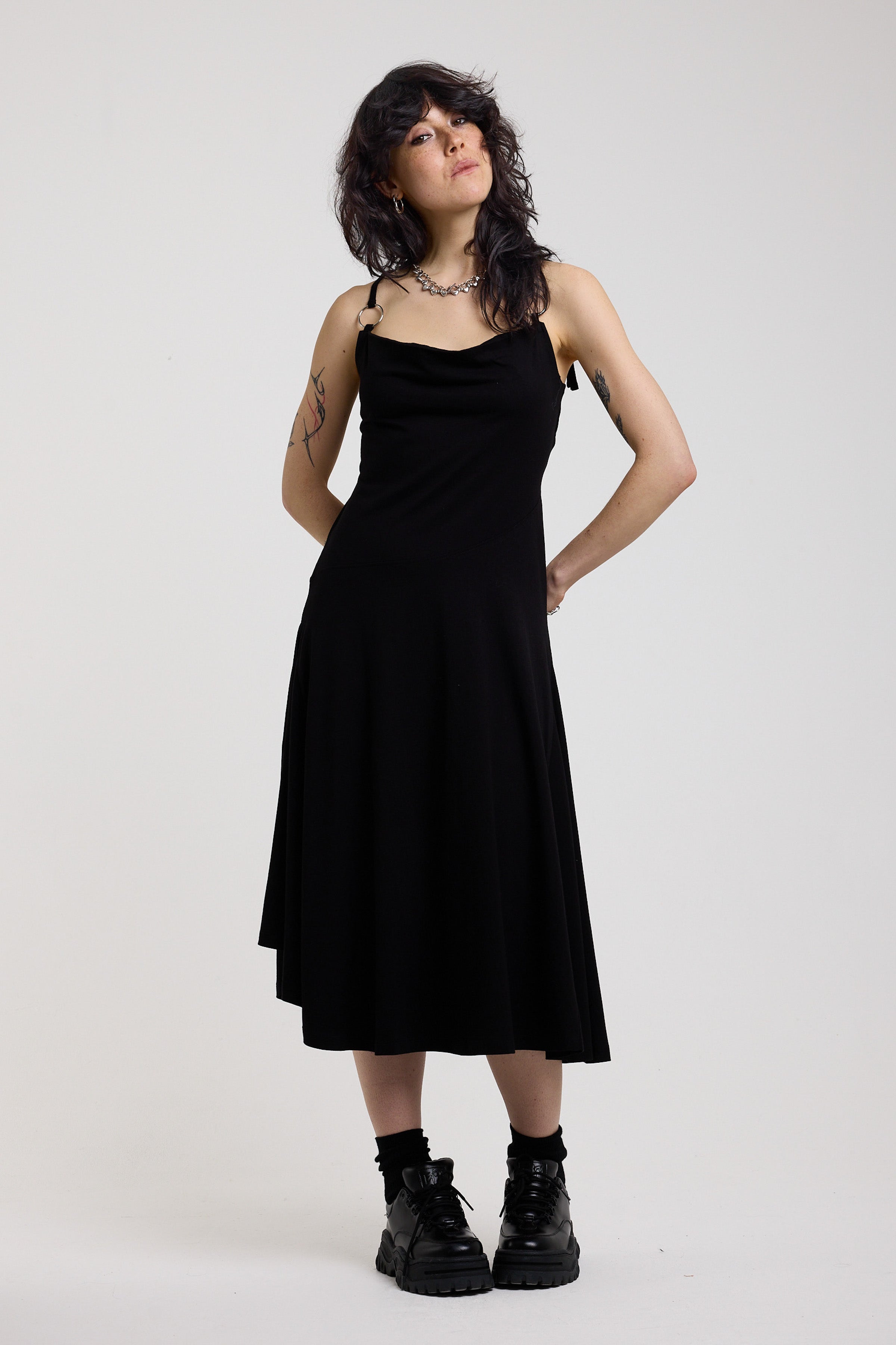 Black slinky midi maxi dress with cowl neck, draped open back, silver O-rings and strappy tie straps, worn by model