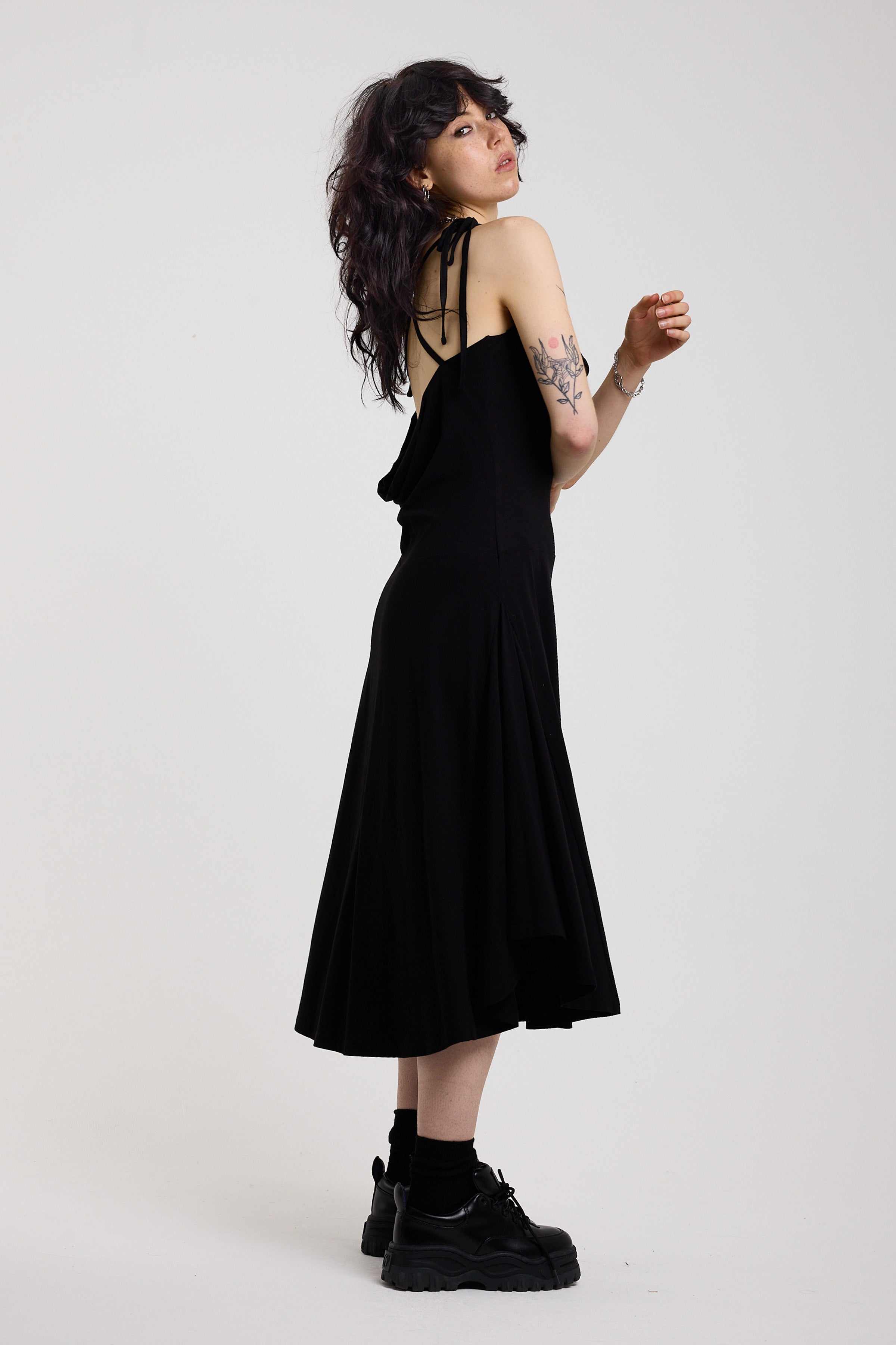 Black slinky midi maxi dress with cowl neck, draped open back, silver O-rings and strappy tie straps, worn by model