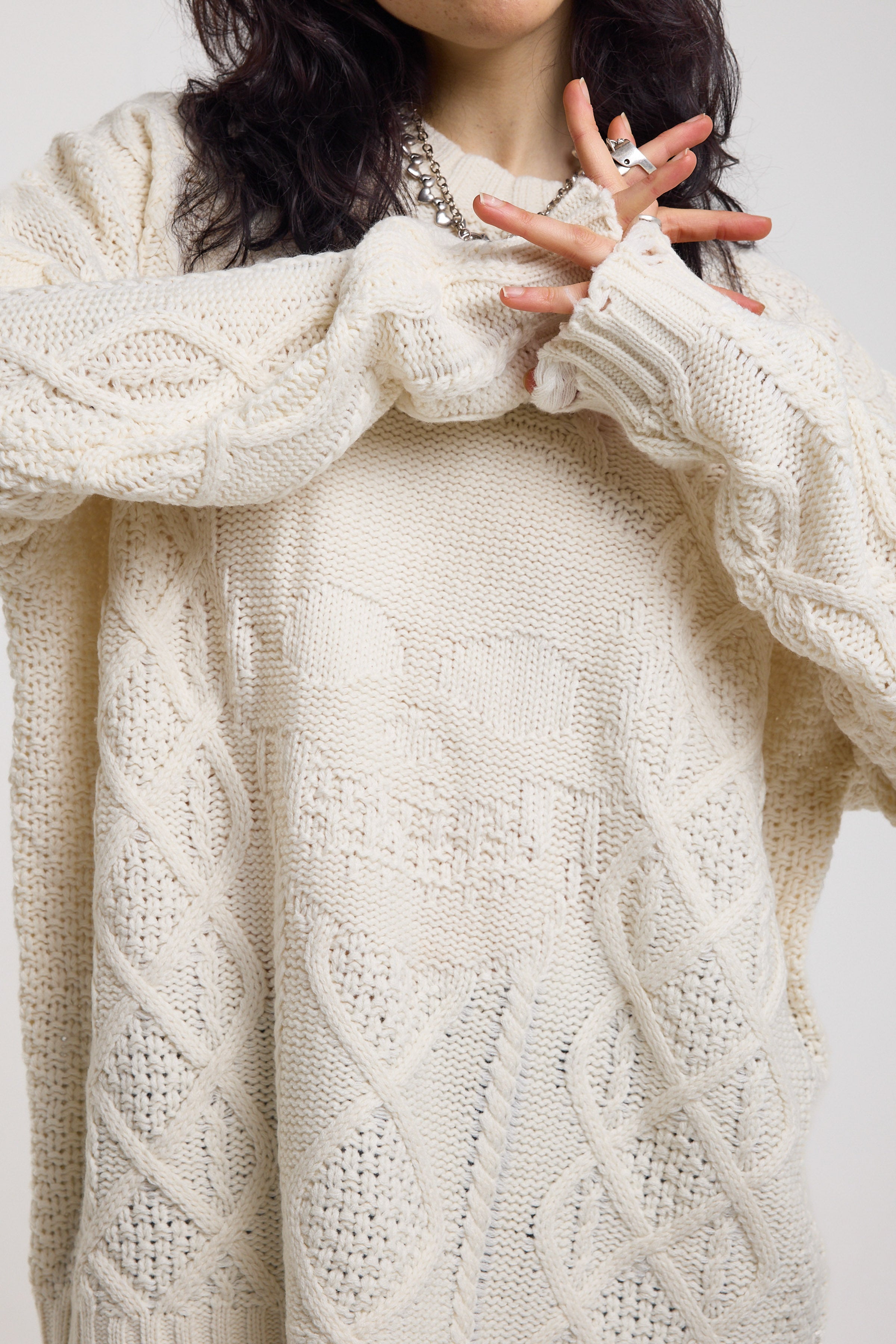 Close up of cream oversized cable knit jumper with skull motif and distressed details, worn by model