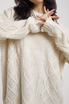 Close up of cream oversized cable knit jumper with skull motif and distressed details, worn by model