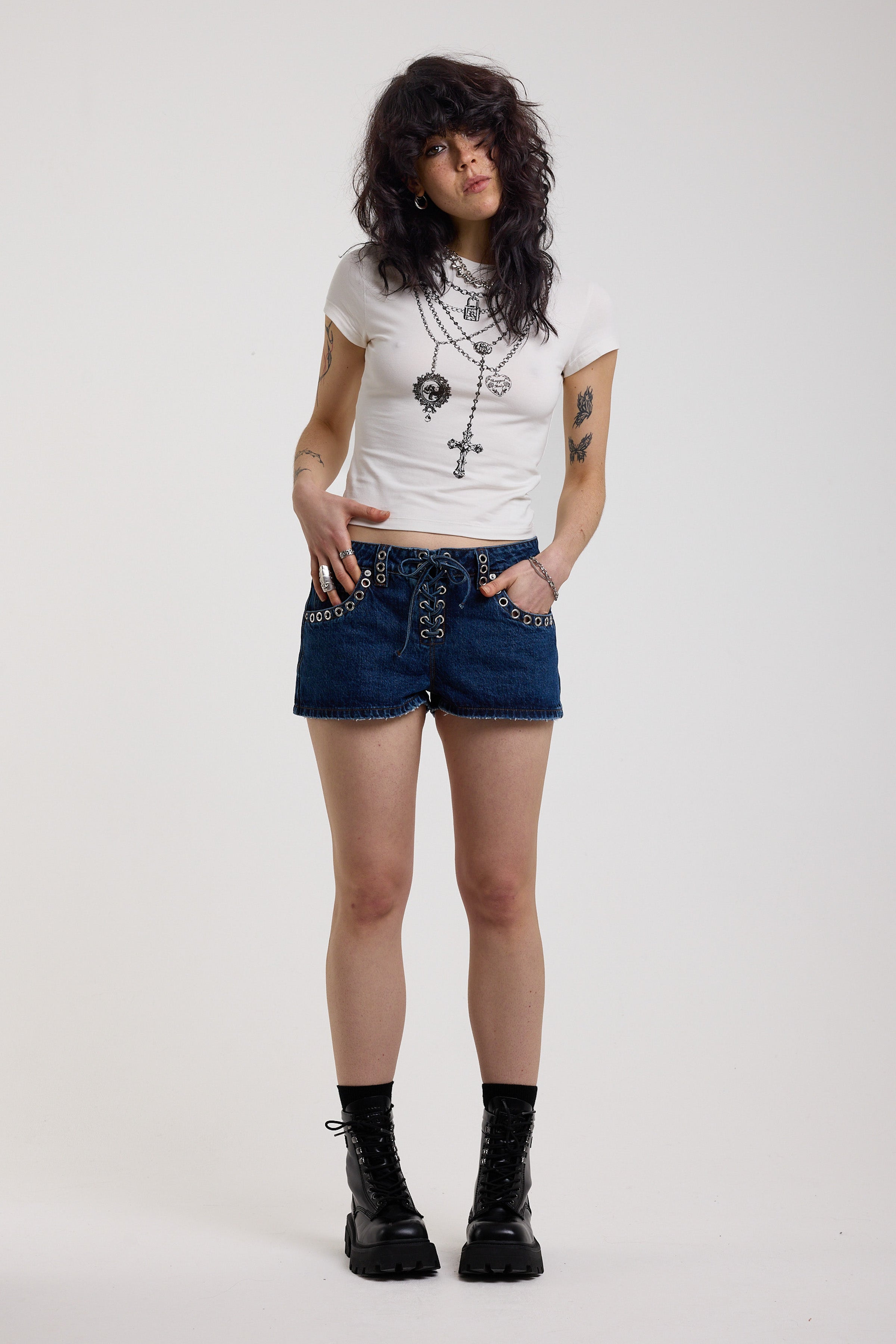 Dark rinse denim hotpants with silver eyelet grommet studs and lace up front detail, worn by model