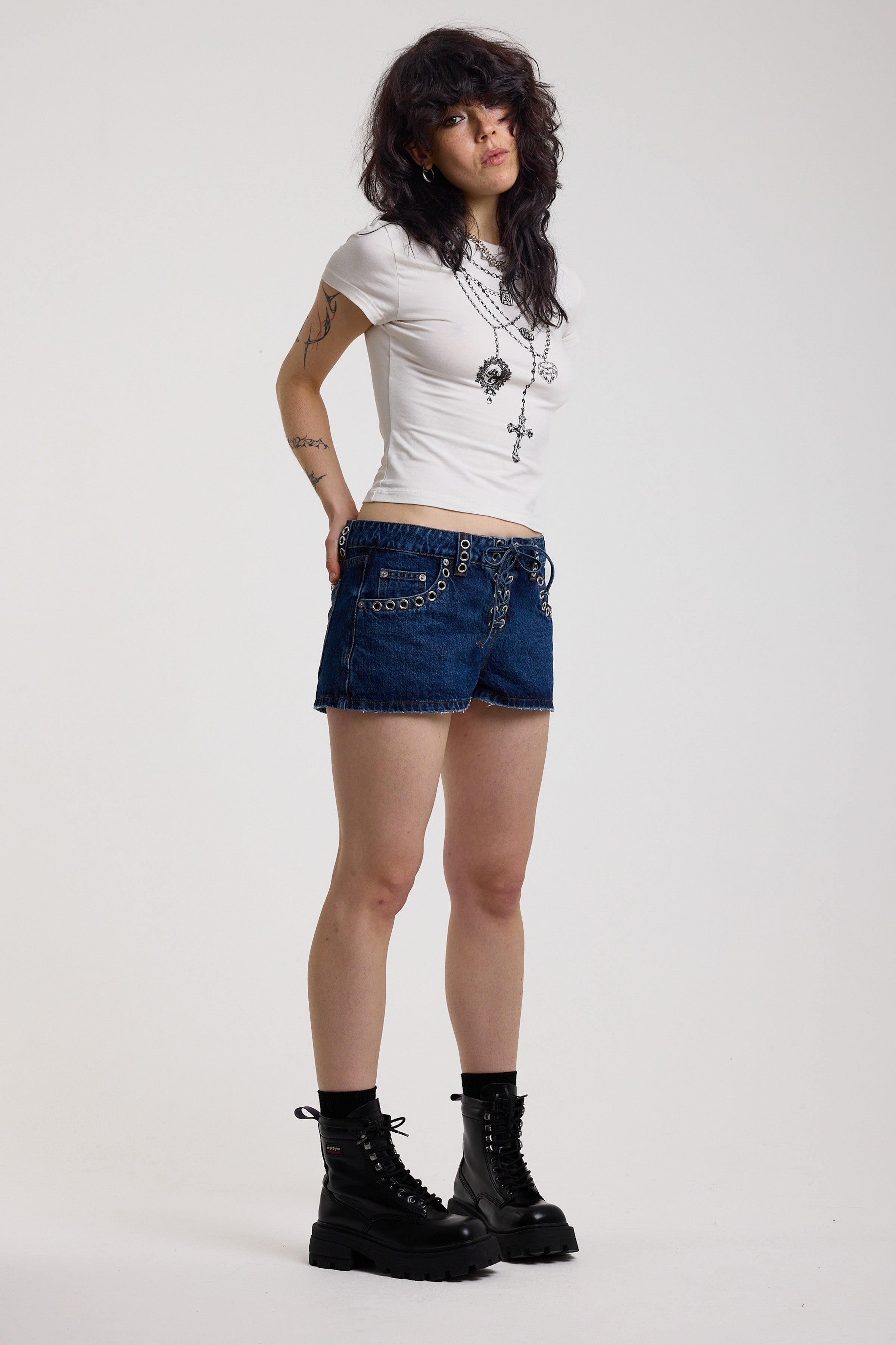 Dark rinse denim hotpants with silver eyelet grommet studs and lace up front detail, worn by model