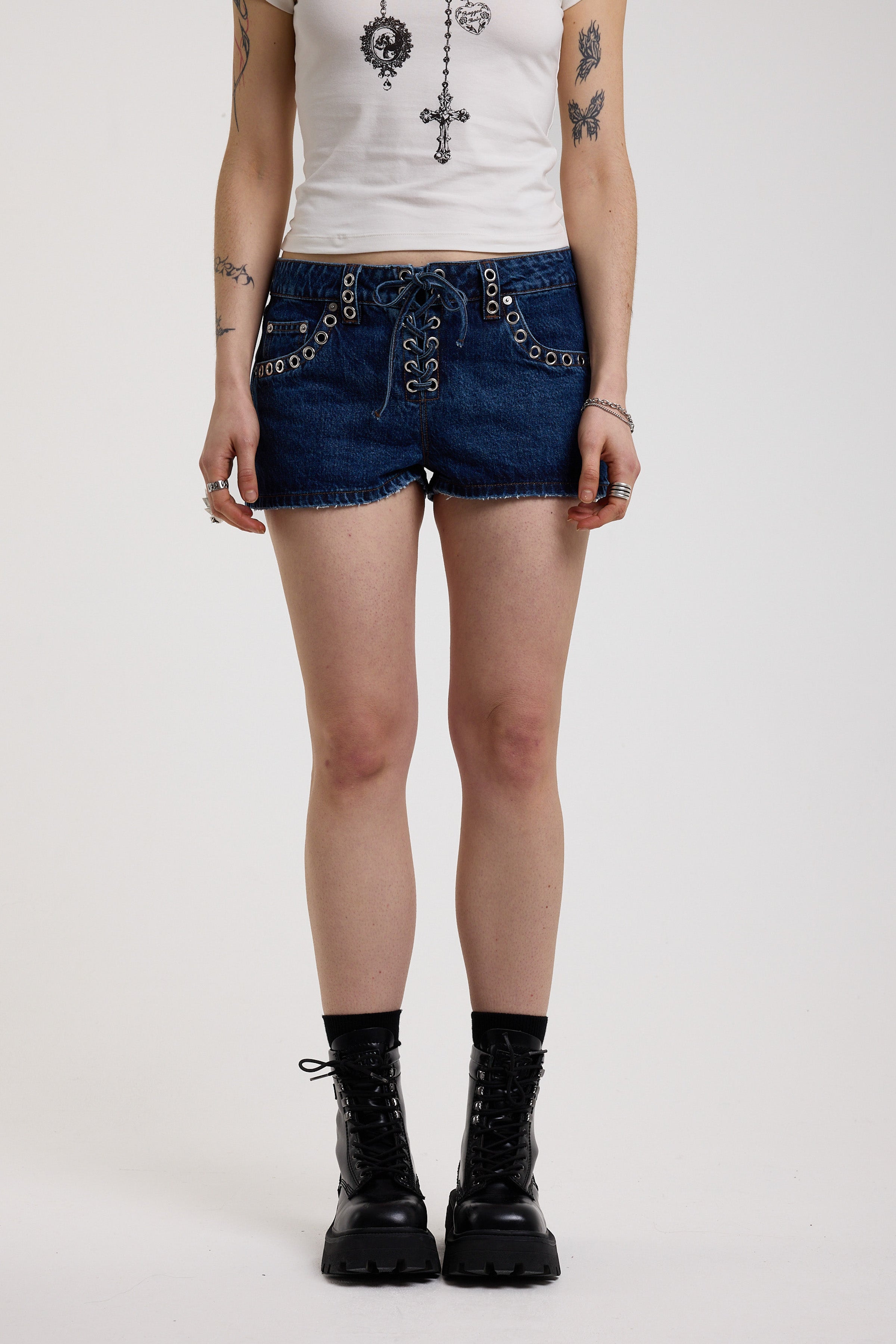 Dark rinse denim hotpants with silver eyelet grommet studs and lace up front detail, worn by model