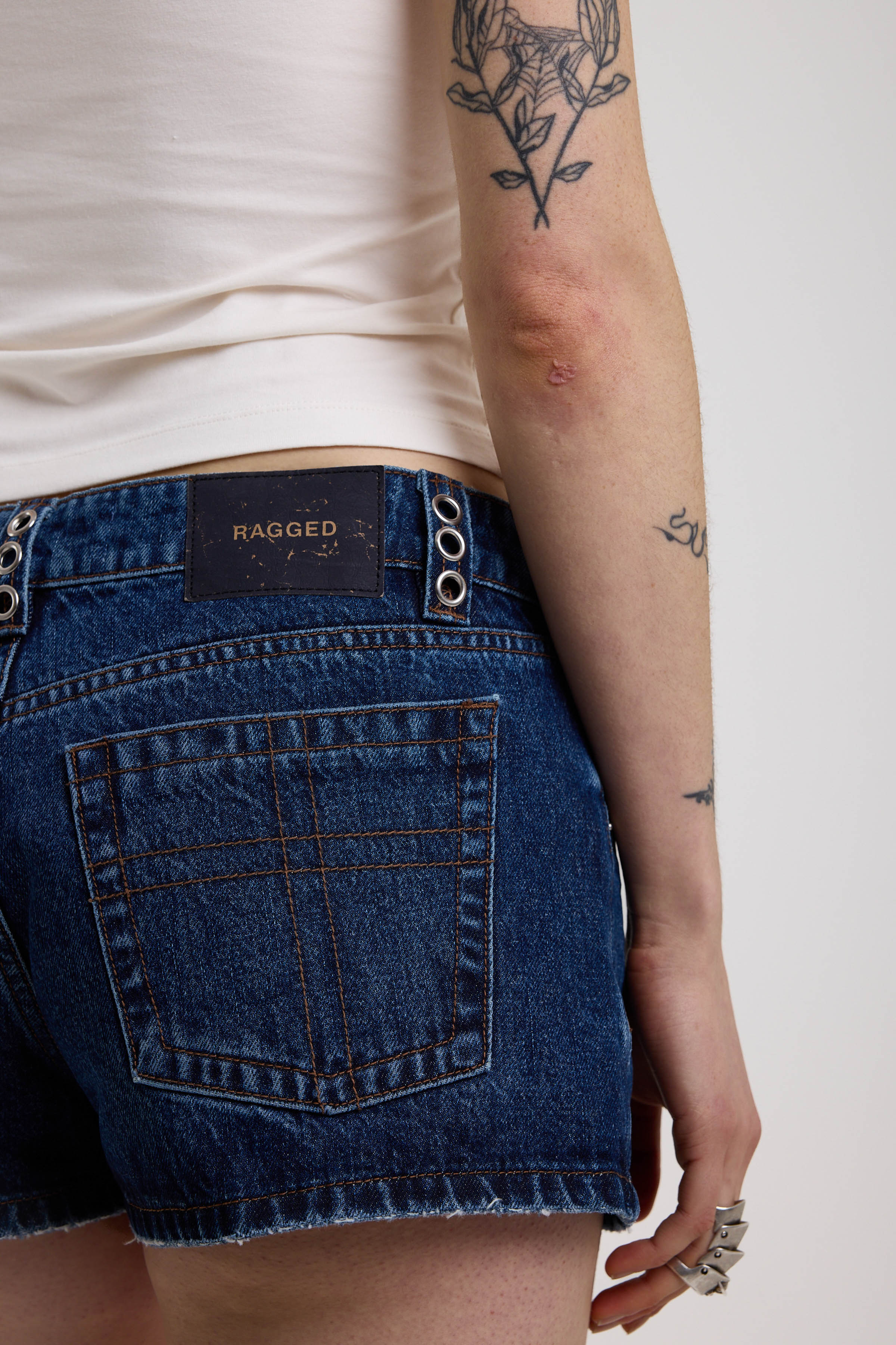 Dark rinse denim hotpants with silver eyelet grommet studs and lace up front detail, worn by model