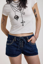 Dark rinse denim hotpants with silver eyelet grommet studs and lace up front detail, worn by model