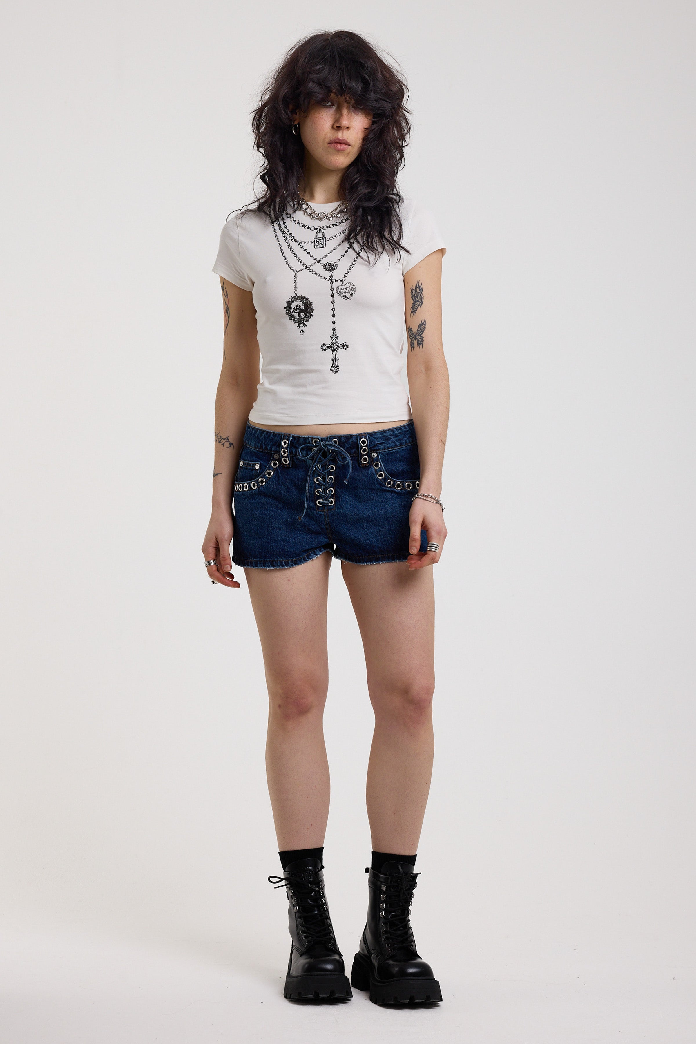 Dark rinse denim hotpants with silver eyelet grommet studs and lace up front detail, worn by model