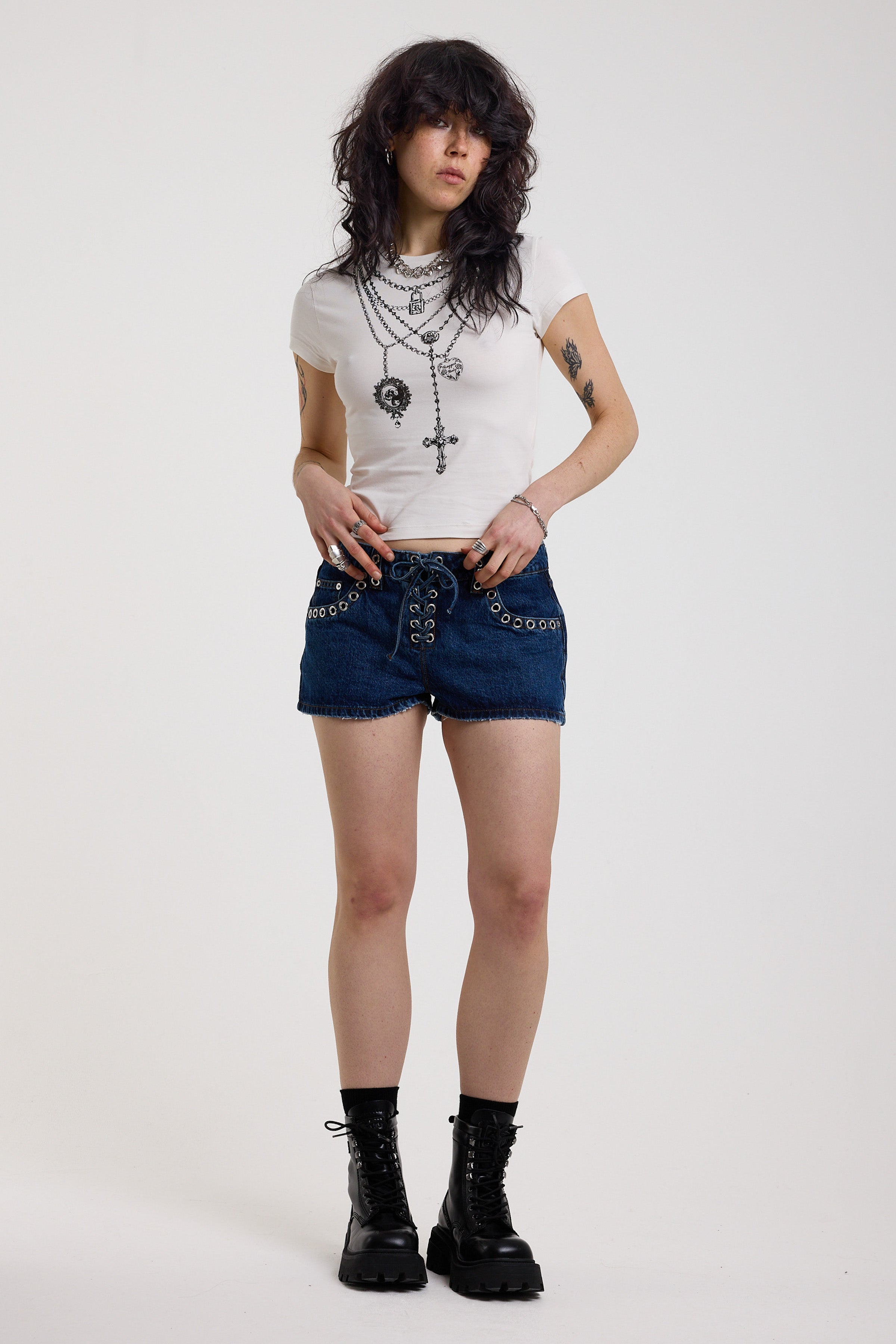Dark rinse denim hotpants with silver eyelet grommet studs and lace up front detail, worn by model