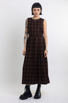 Burgundy check pinafore midi dress with pleated skirt with silver D-ring hardware, worn by model