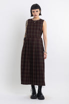 Burgundy check pinafore midi dress with pleated skirt with silver D-ring hardware, worn by model