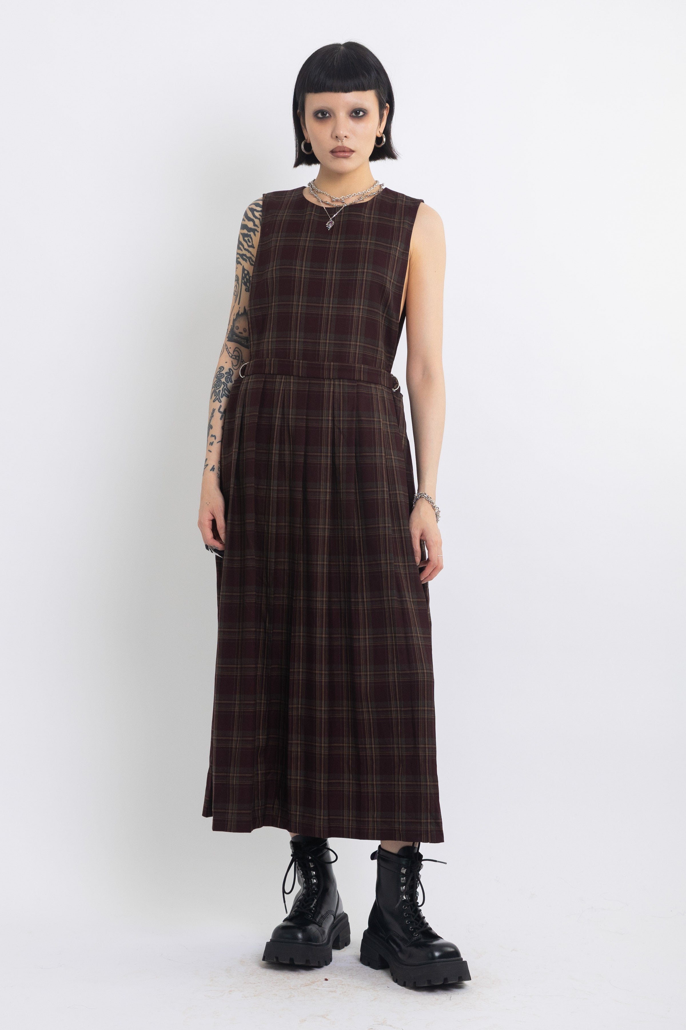 Burgundy check pinafore midi dress with pleated skirt with silver D-ring hardware, worn by model