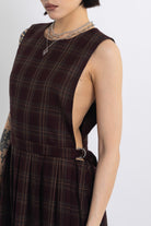Burgundy check pinafore midi dress with pleated skirt with silver D-ring hardware, worn by model