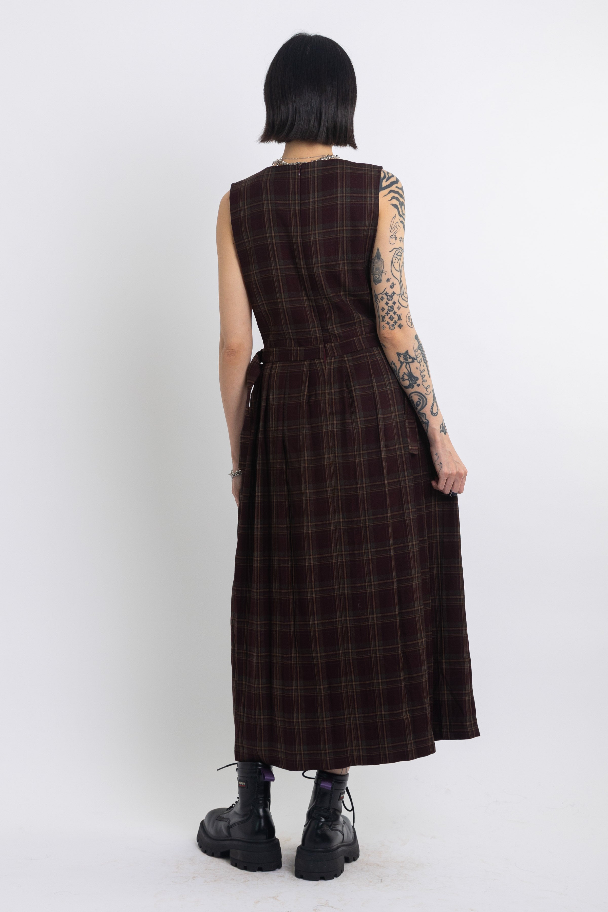 Burgundy check pinafore midi dress with pleated skirt with silver D-ring hardware, worn by model