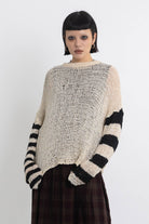 Ecru open knit jumper with asymmetric black stripe sleeves, worn by model