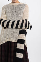 Ecru open knit jumper with asymmetric black stripe sleeves, worn by model