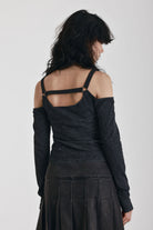 Washed black long-sleeve cold-shoulder top with cutout eyelet straps and silver buckles, worn by model
