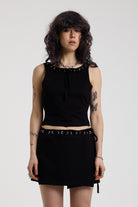 Black slash neck open back tank top with silver eyelet detail, worn by model