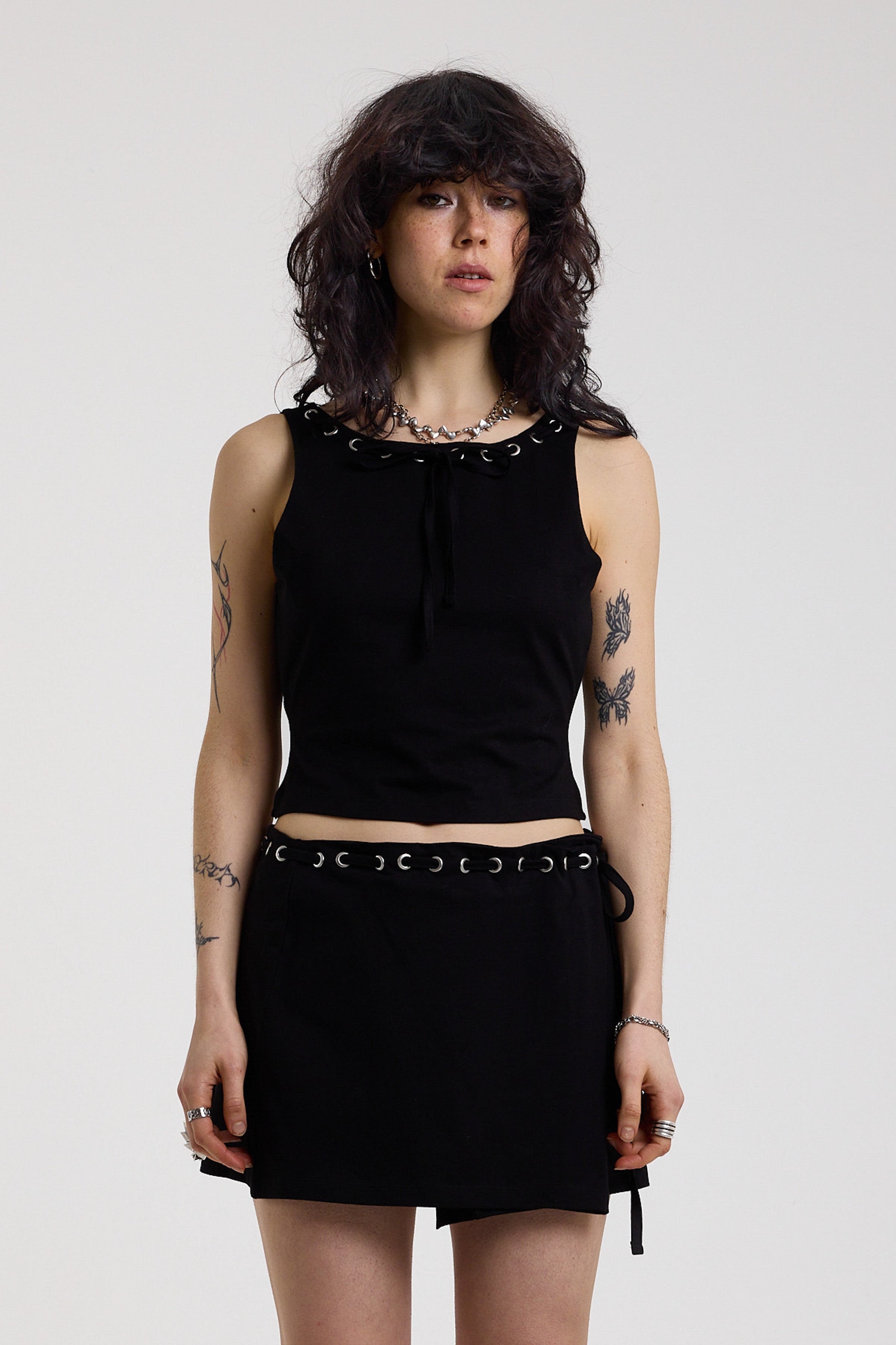 Black slash neck open back tank top with silver eyelet detail, worn by model