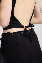 Black slash neck open back tank top with silver eyelet detail, worn by model